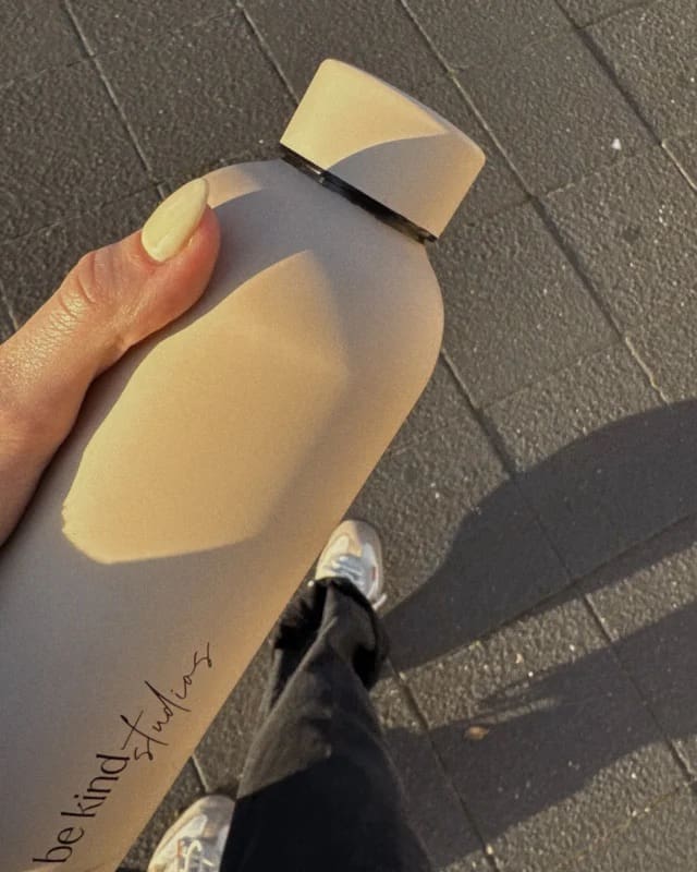 person holding be kind studios water bottle while walking